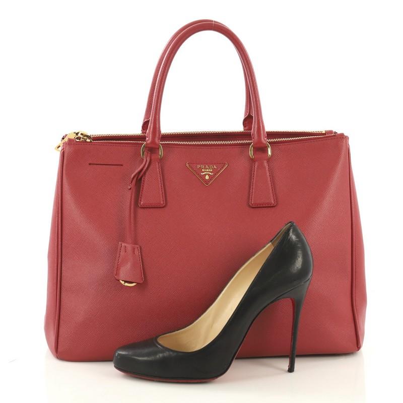 This Prada Double Zip Lux Tote Saffiano Leather Medium, crafted from red saffiano leather, features dual rolled handles, raised Prada logo plate, and gold-tone hardware. It opens to a red fabric interior with two zip compartments on both sides and