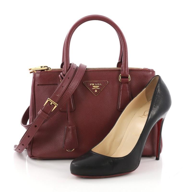 This Prada Double Zip Lux Tote Saffiano Leather Small, crafted from burgundy saffiano leather, features side snap buttons, raised Prada logo plate, dual rolled leather handles, and gold-tone hardware. It opens to a burgundy fabric interior with two