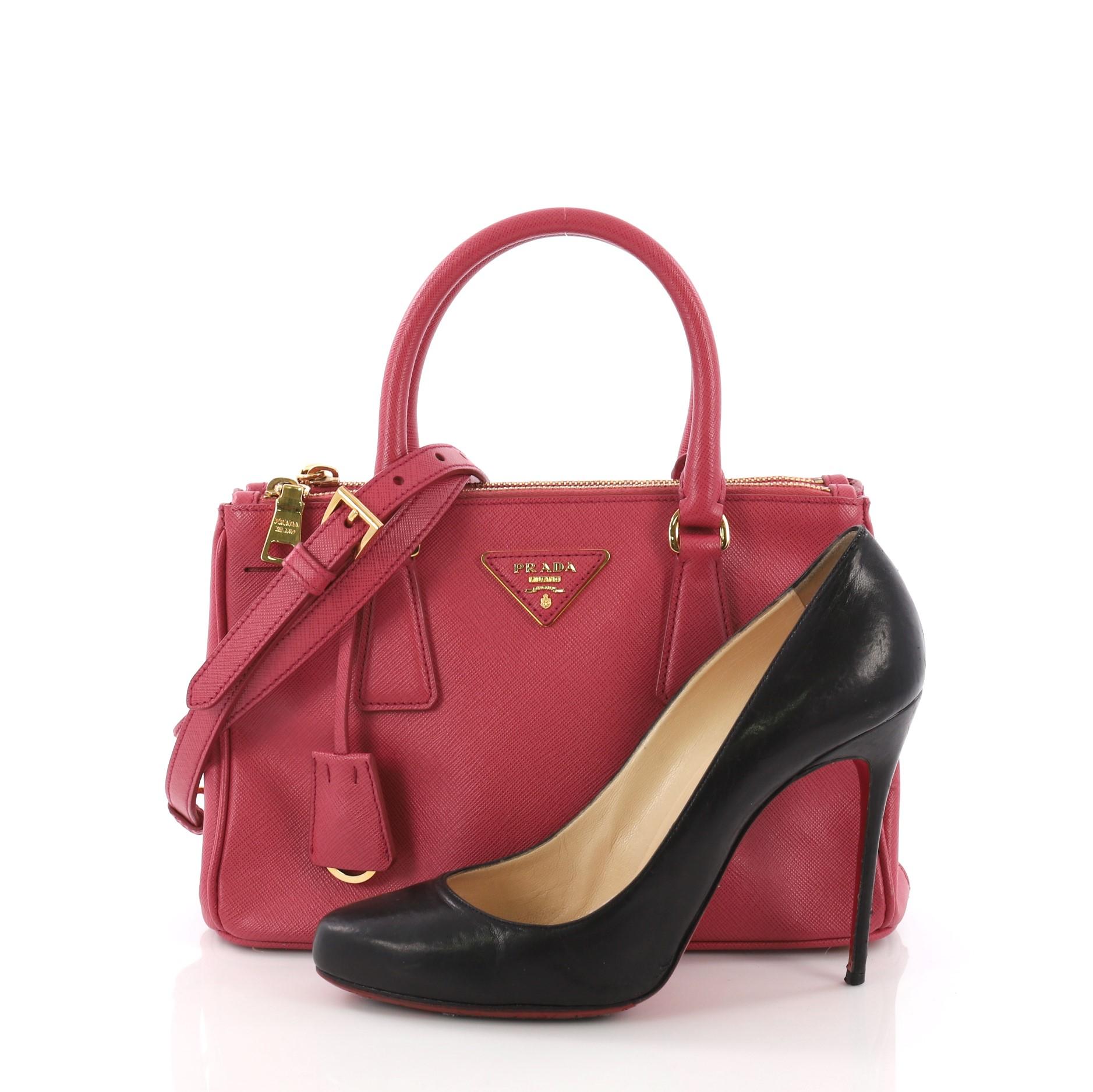This Prada Double Zip Lux Tote Saffiano Leather Small, crafted from pink saffiano leather, features dual rolled handles, raised Prada logo plate, and gold-tone hardware. It opens to a pink fabric interior with two zip compartments on both sides and