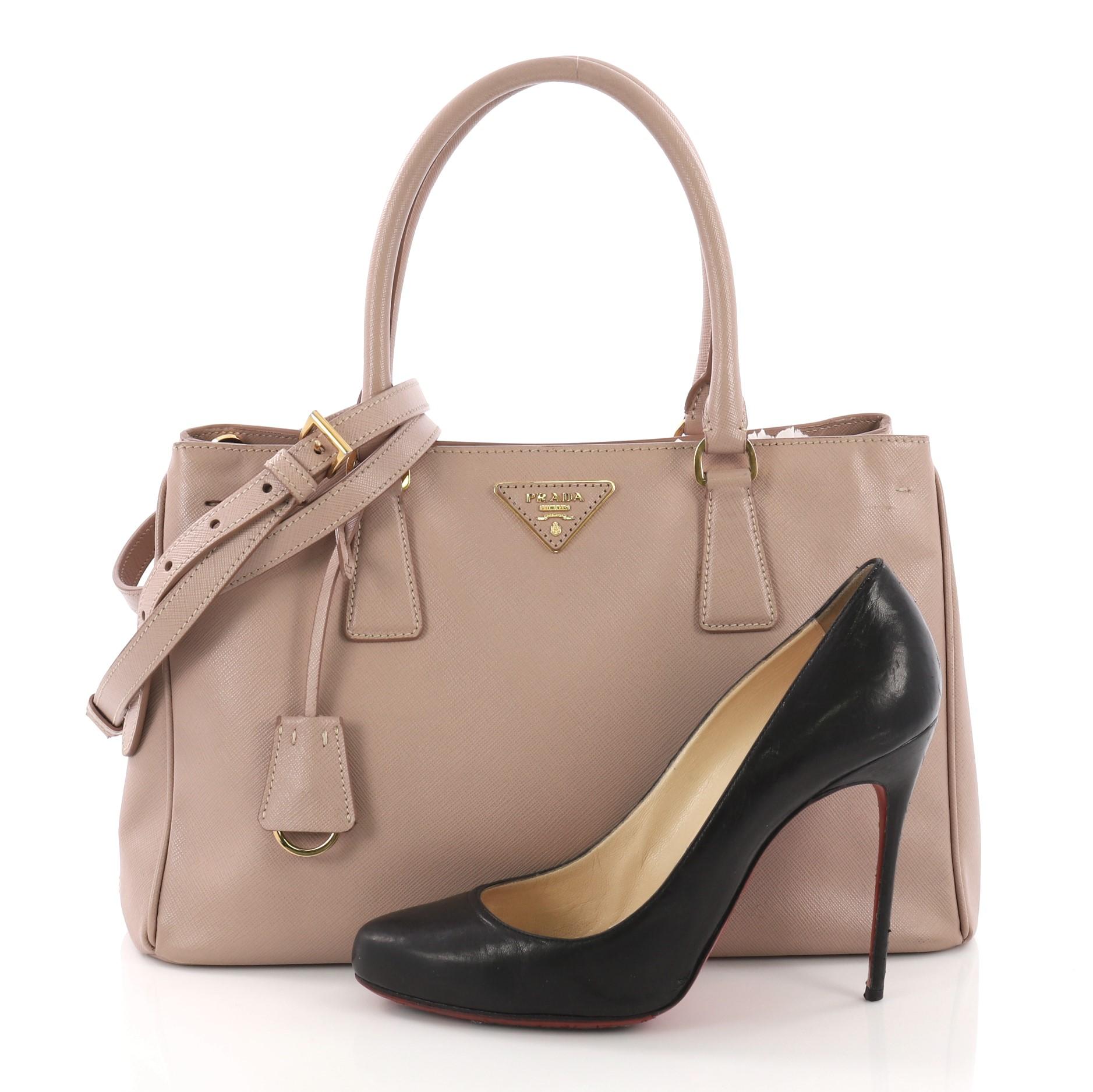 This Prada Double Zip Lux Tote Saffiano Leather Small, crafted from pink saffiano leather, features dual rolled handles, raised Prada logo plate, and gold-tone hardware. It opens to a beige fabric interior with two zip compartments on both sides and
