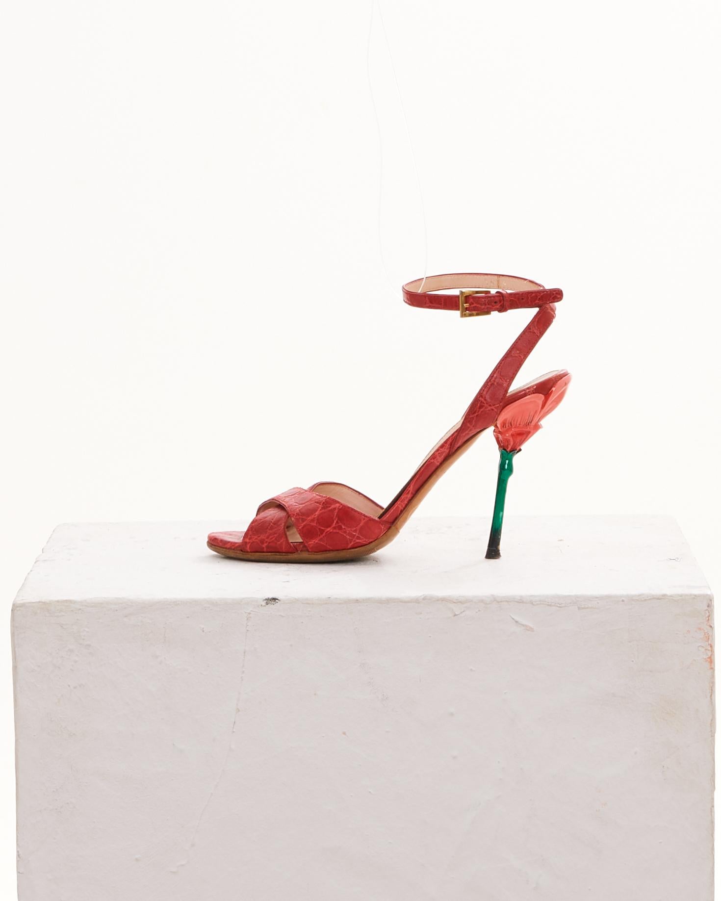 - Prada
- Early 2000s Collection
- Strawberry red crocodile-embossed leather sandals
- Cross-strap open-toe design
- Slim ankle strap with a gold-tone adjustable buckle
- Contrasting green stiletto heel for a unique and striking appearance
-