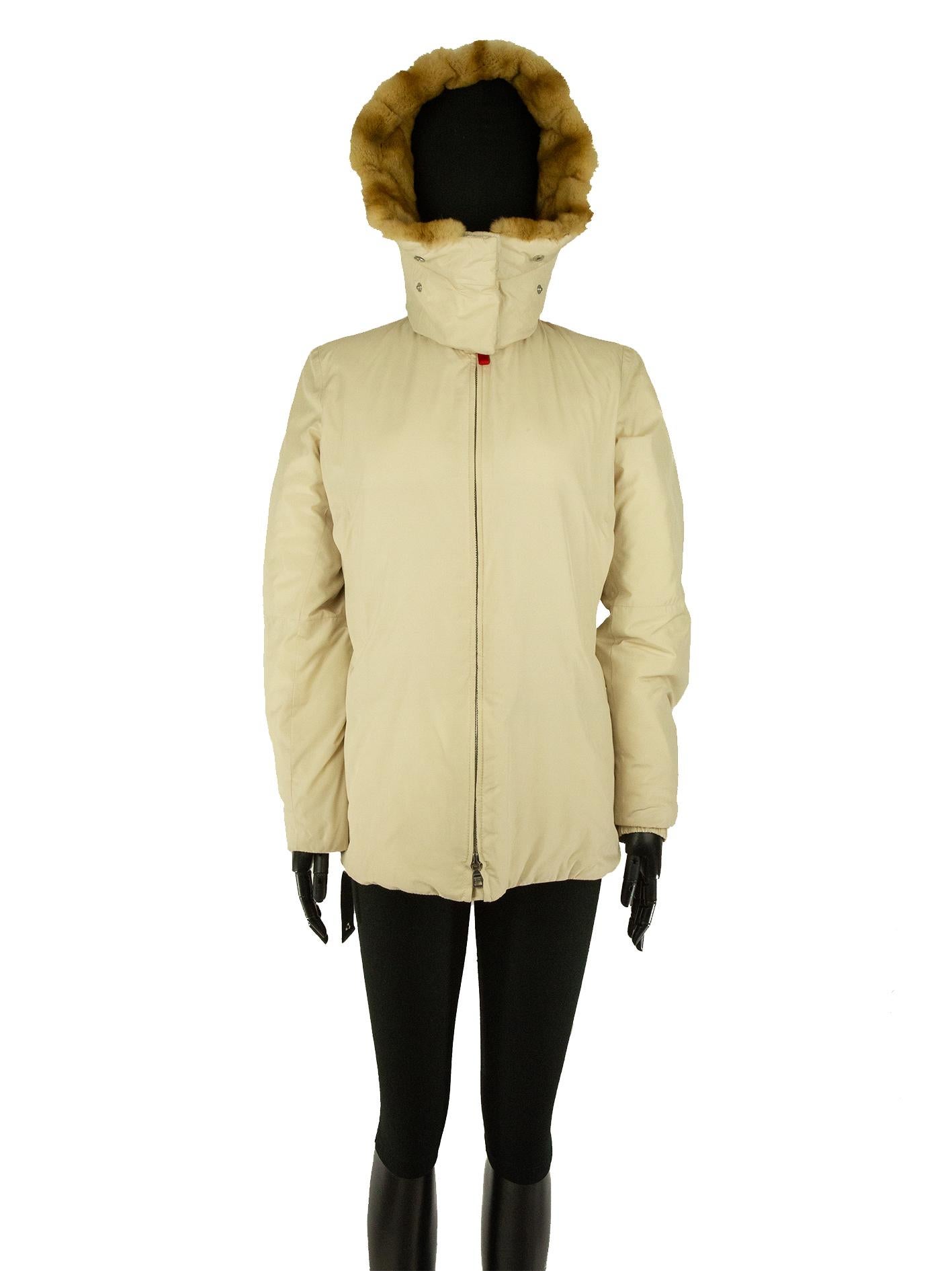 A Prada coat in ecru, filled with polyester down. The fur-trimmed hood, made of dyed kolinski fur, is attached to a wool collar and is fully detachable. Inside of the coat contains a zip on the back lining making the jacket making it foldable and