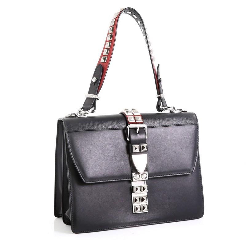 This Prada Elektra Shoulder Bag Studded Leather Medium, crafted in black studded leather, features leather shoulder strap, studded front buckle, snap-lock closure and silver-tone hardware. Its snap closure opens to a black leather interior with zip