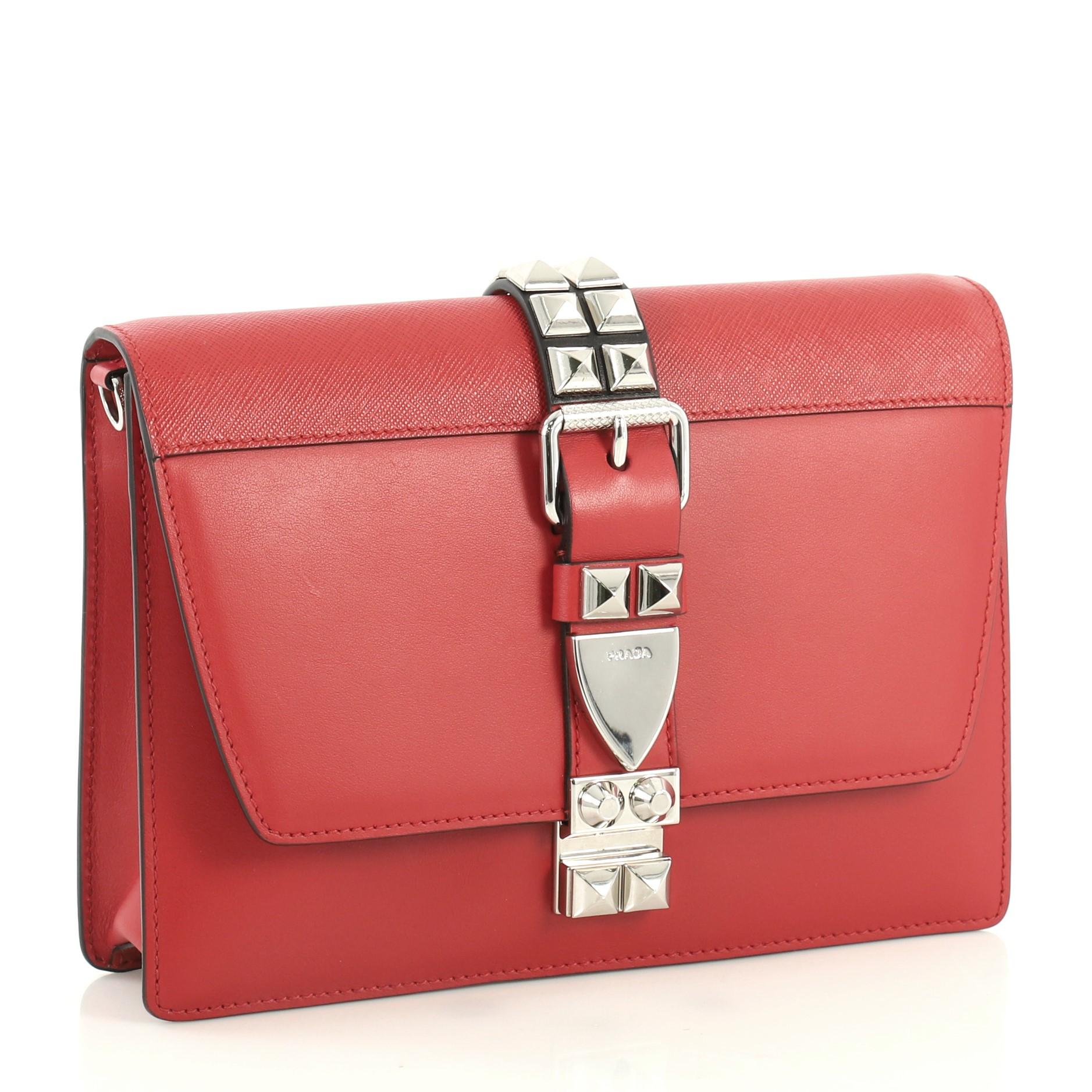 This Prada Elektra Shoulder Bag Studded Leather Small, crafted in red studded leather, features leather shoulder strap, studded front buckle and silver-tone hardware. Its snap-lock closure opens to a red leather and black fabric interior with zip