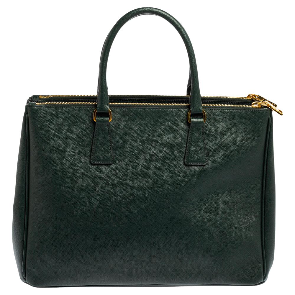 This Double Zip tote by Prada will be a loved addition to your closet. It has been crafted from Saffiano lux leather and styled with gold-tone hardware. It comes with two top handles, two zip compartments, and a perfectly-sized main compartment. The