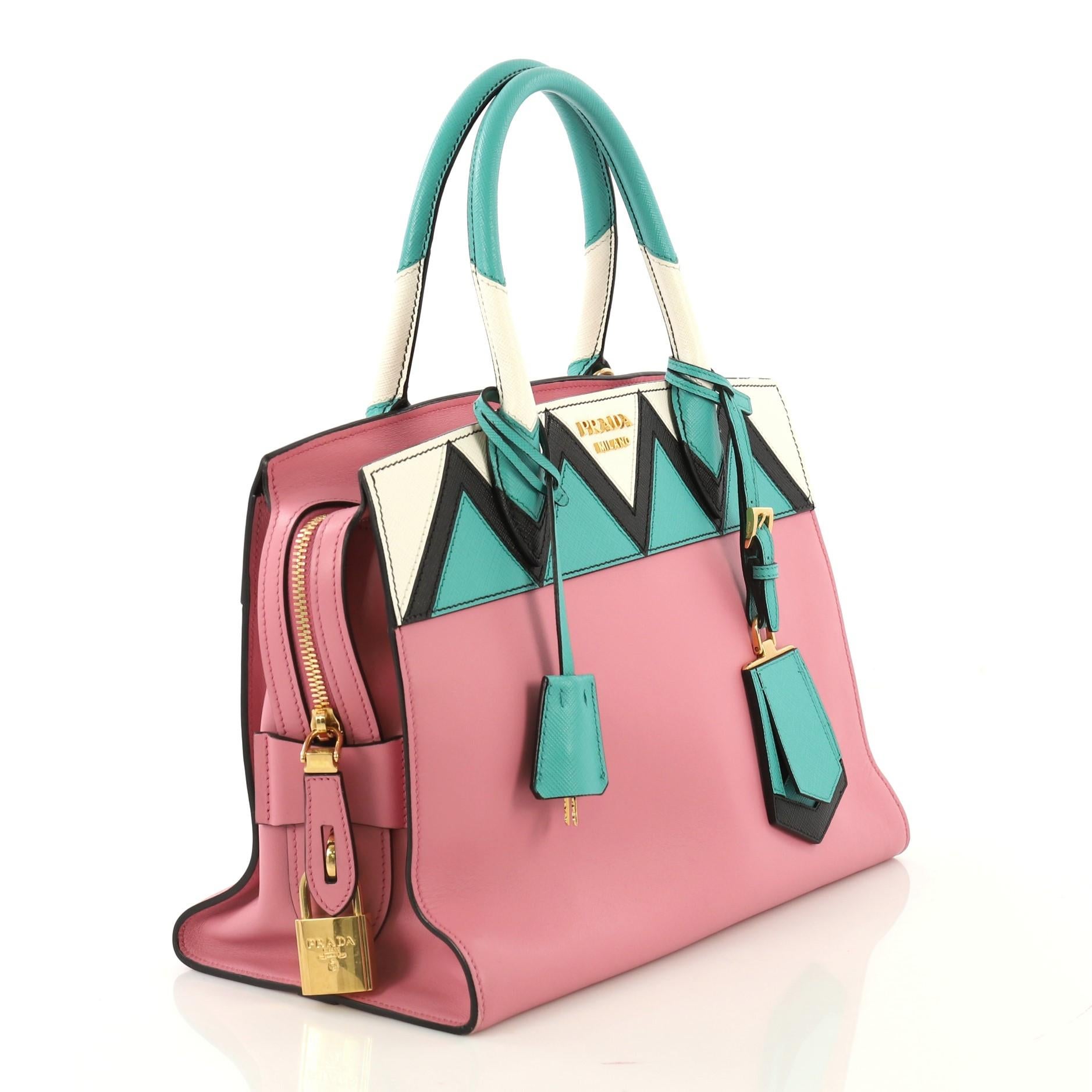 This Prada Esplanade Bag Greca Saffiano with City Calf Medium, crafted in pink saffiano leather with city calfskin, features dual-rolled leather handles, Prada metal logo at center and gold-tone hardware. Its zip closure opens to a black fabric