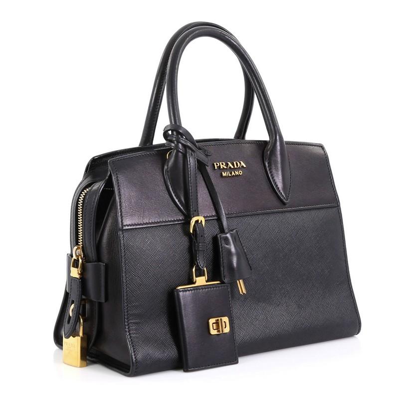 This Prada Esplanade Bag Saffiano Leather Small, crafted from black saffiano leather, features dual rolled leather handles, signature Prada logo at top center, and gold-tone hardware. Its zip closure opens to a black fabric and leather interior with