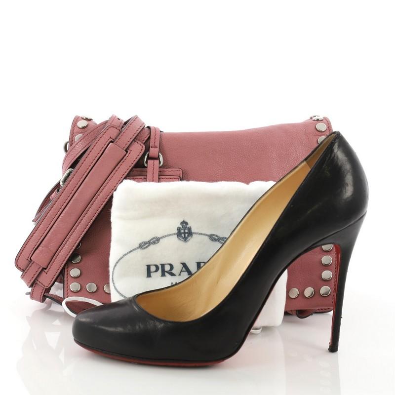 This Prada Etiquette Flap Bag Studded Glace Calfskin Small, crafted from pink studded glace calfskin leather, features a detachable shoulder strap, two side zip compartments, and silver-tone hardware. It opens to a blue suede interior divided into