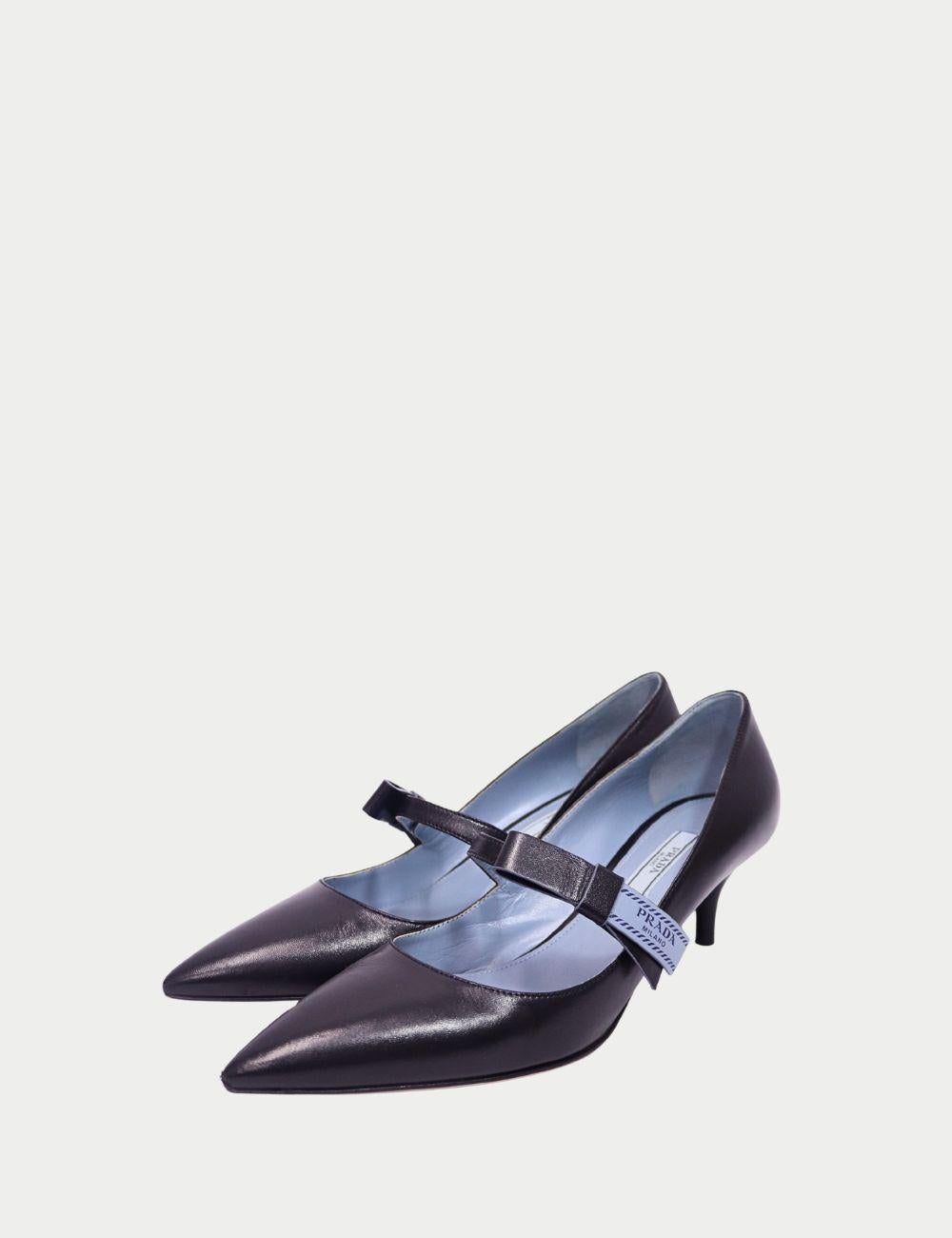Desprende elegancia con estos zapatos de salón Prada, confeccionados en suave piel negra con una elegante punta afilada y un fino tacón de media altura. Con una moderna tira en el empeine con el logotipo de Prada Milano, estos tacones combinan la