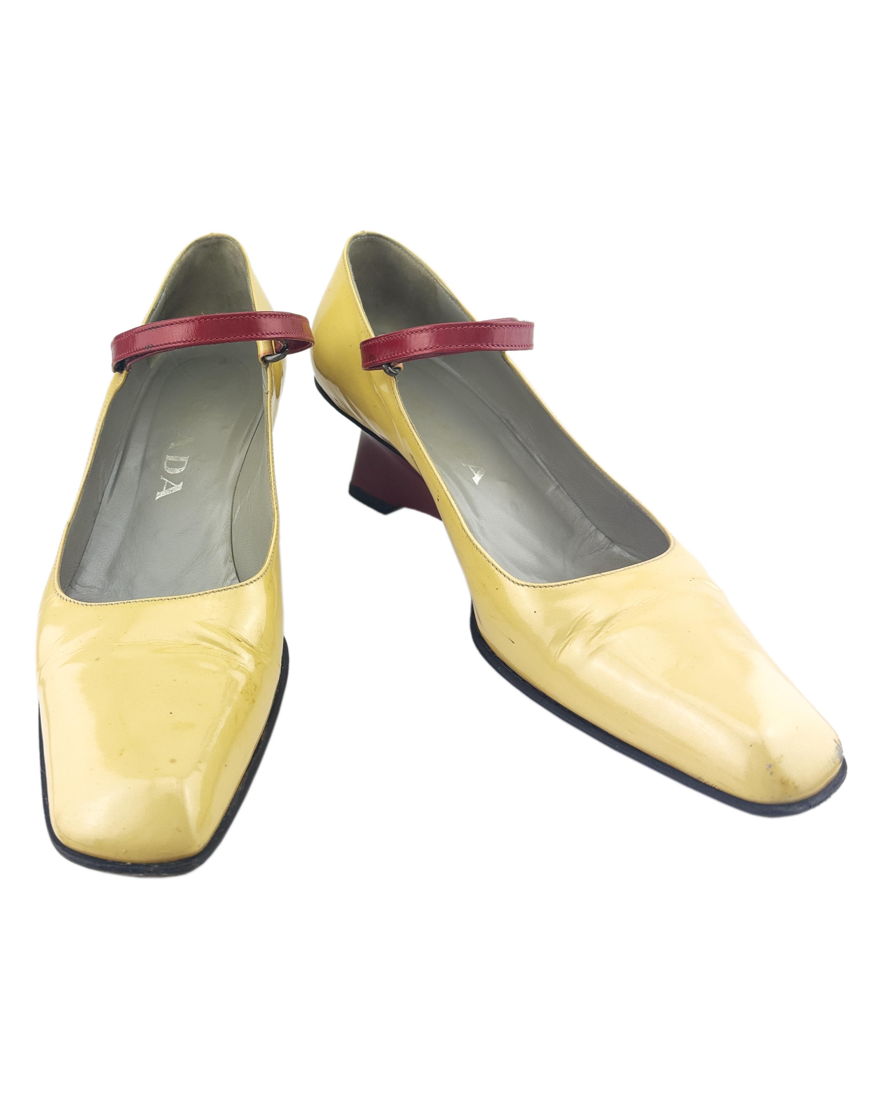 Prada Mary Janes from the Fall/Winter 1998 collection. Butter yellow/beige patent leather body with contrasting dark red velcro strap and structural wedge heel. Slanted square toe and black rubber exterior sole. The white and red version were