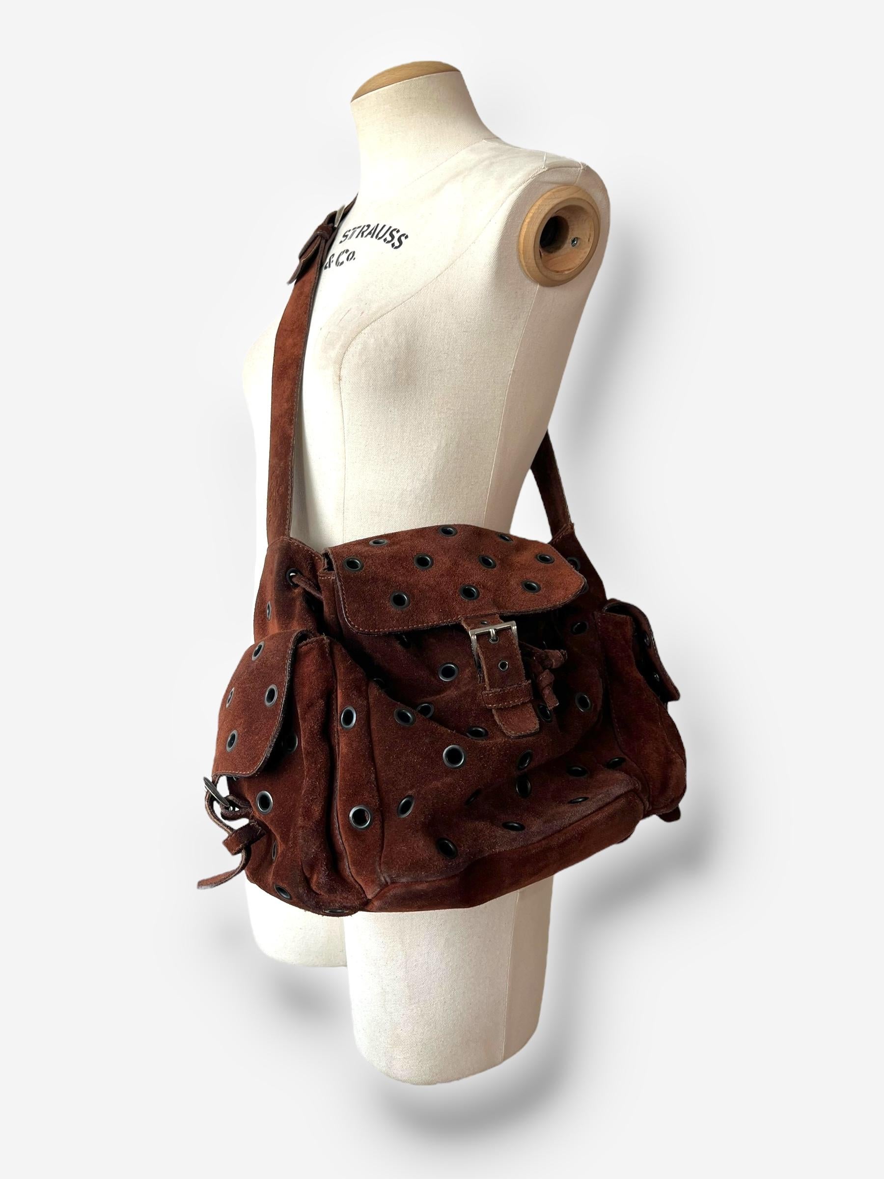 
De la colección Otoño/Invierno 1999 de Prada, este distintivo bolso bandolera está fabricado en ante marrón y adornado con ojales de ojal. Incluye un asa con el logotipo de Prada en relieve, correa ajustable, un bolsillo interior y dos bolsillos
