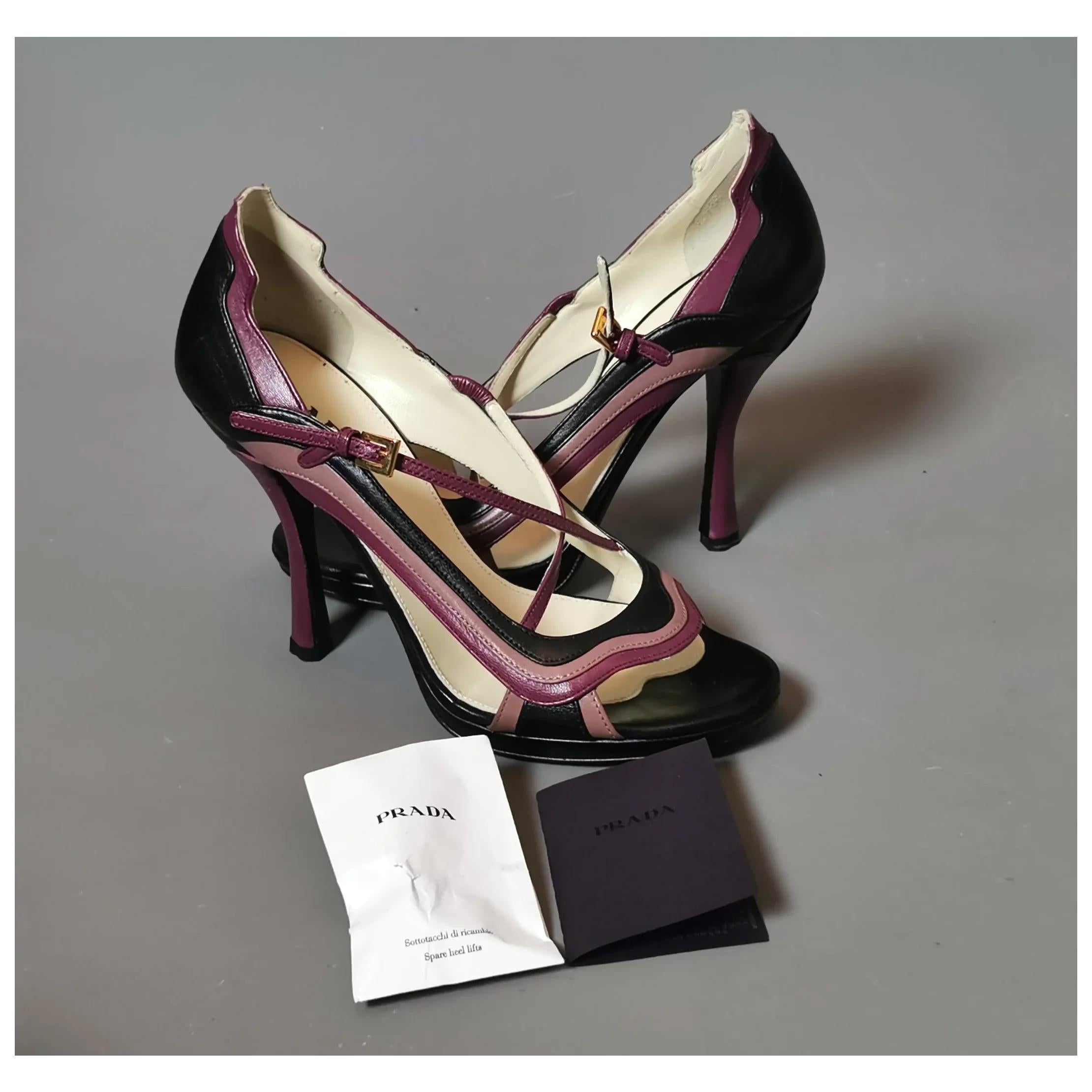 A stunning pair of Prada 'Fairy Garden' Jane stiletto heel shoes.

Black and magenta coloured leather cut out heels with a wave design.

They have tall stiletto heels and a Crossover strap that fastens with a gold tone buckle, the shoes have a peep