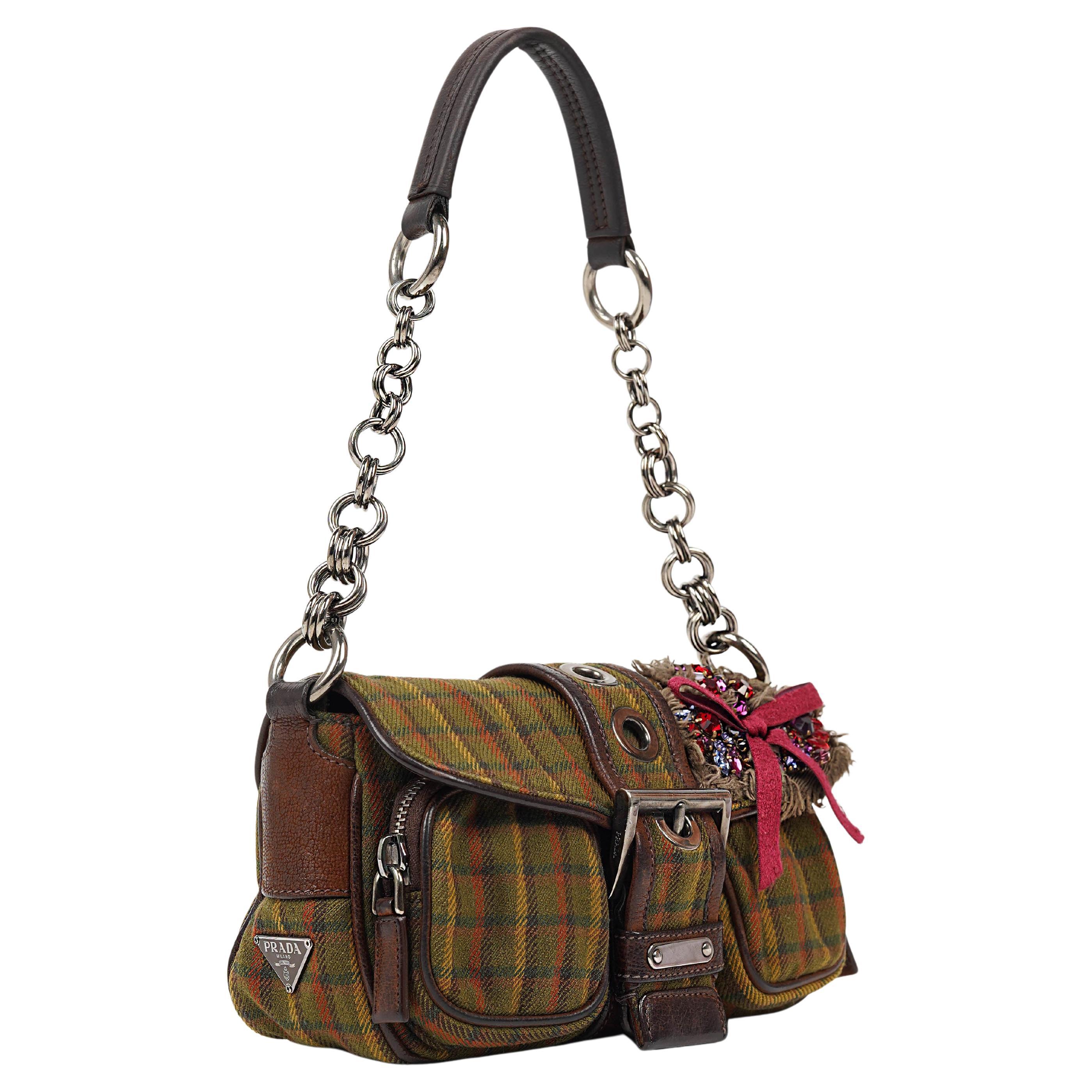 From Prada’s highly collectible Fall/Winter 2004 collection, this striking tartan mini shoulder bag captures the house’s unique balance of utility and ornamentation. Crafted in Italy, the piece features a bold green and red plaid wool body, trimmed