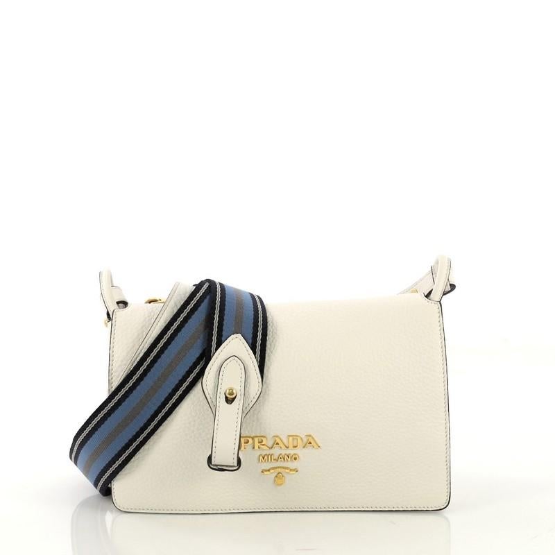 This Prada Flap Crossbody Bag Vitello Daino Small, crafted in white vitello daino leather, features an adjustable shoulder strap, exterior back zip compartment, front flap with raised Prada logo, and gold-tone hardware. Its magnetic closure opens to