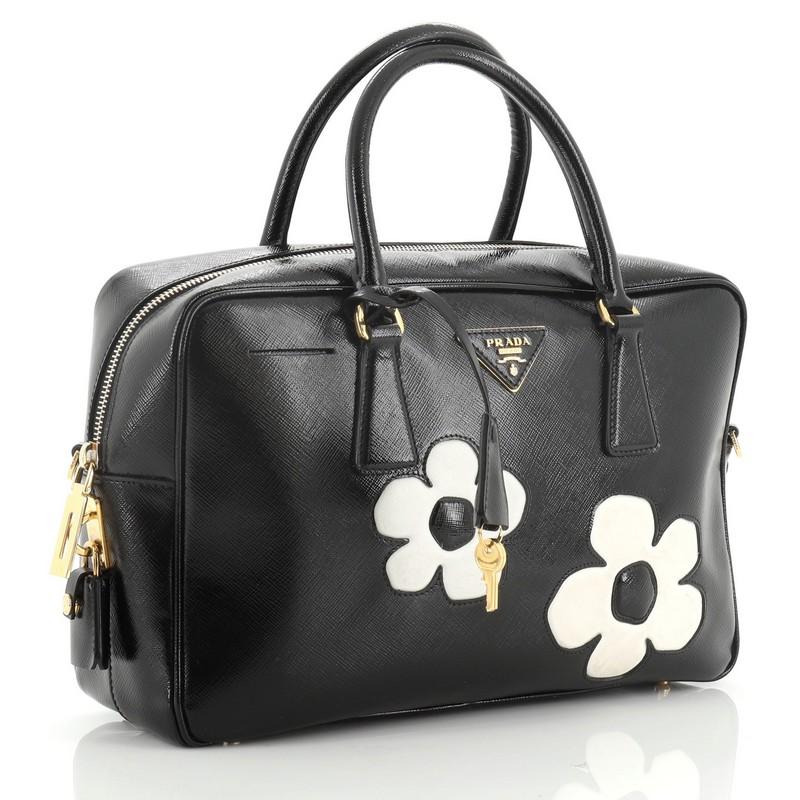 This Prada Flowers Bauletto Bag Vernice Saffiano Leather Medium is an everyday bag ideal for carrying your daily essentials with its roomy interior. Crafted from white and black vernice saffiano leather leather, features two white flower applique on