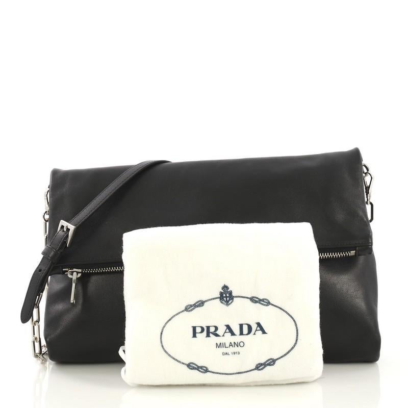 This Prada Fold Over Chain Clutch Soft Calfskin Medium, crafted from black soft calfskin, features silver-tone hardware. Its zip closure opens to a red leather interior. 

Condition: Excellent. Minor wear on base corners, small indentations and