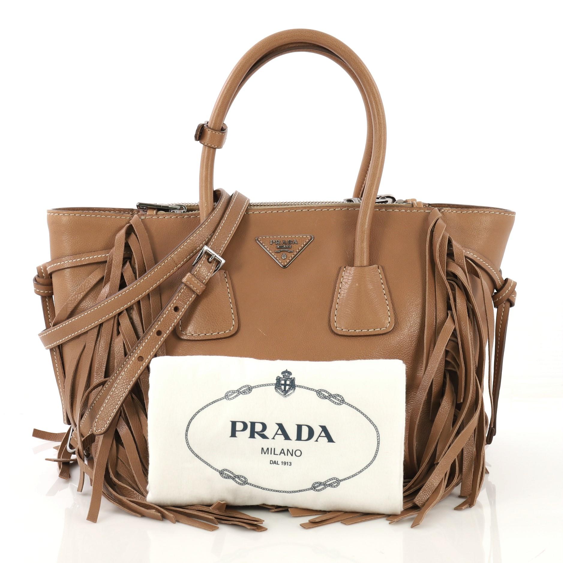 This Prada Fringed Twin Pocket Tote Glace Calf Small, crafted from brown glace calf leather, features dual rolled top handles, center Prada triangle logo, fringed leather detailing, and silver-tone hardware. Its snap closure opens to a brown fabric