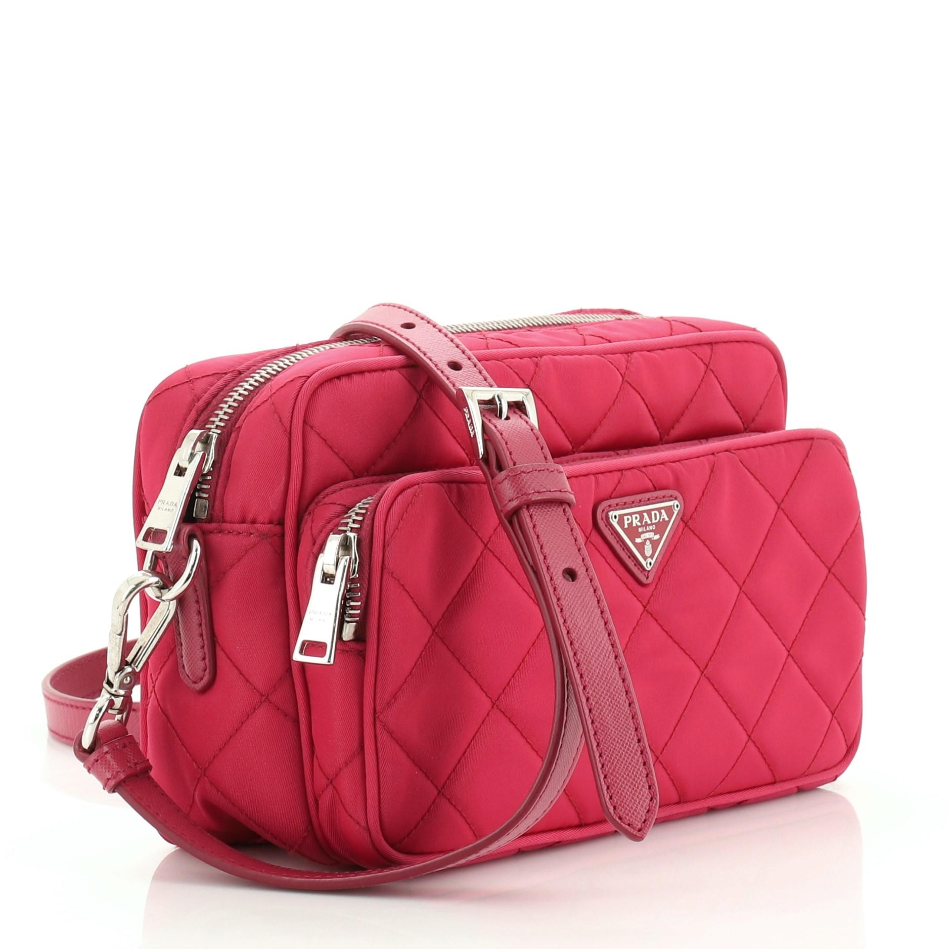 This Prada Front Pocket Camera Bag Quilted Tessuto Small, crafted from pink quilted tessuto, features adjustable leather strap, exterior front zip pocket, and silver-tone hardware. Its top zip closure opens to a pink fabric interior with zip pocket.