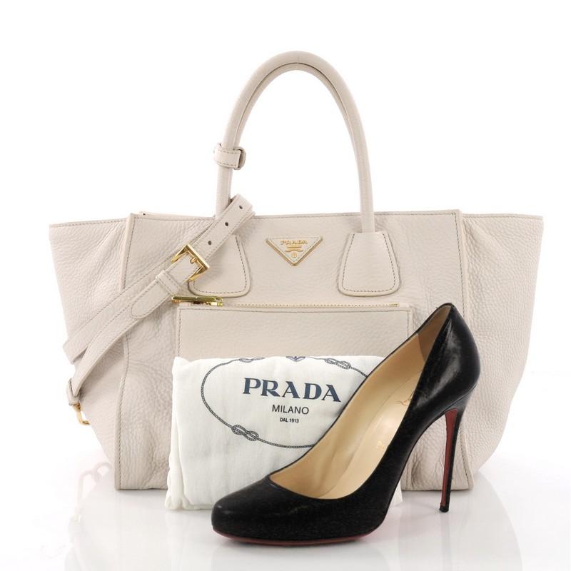This Prada Front Pocket Wing Convertible Tote Vitello Daino, crafted in off-white leather, features dual rolled leather handles, exterior front zip pocket, expandable sides, and gold-tone hardware. Its snap button closure opens to a beige fabric