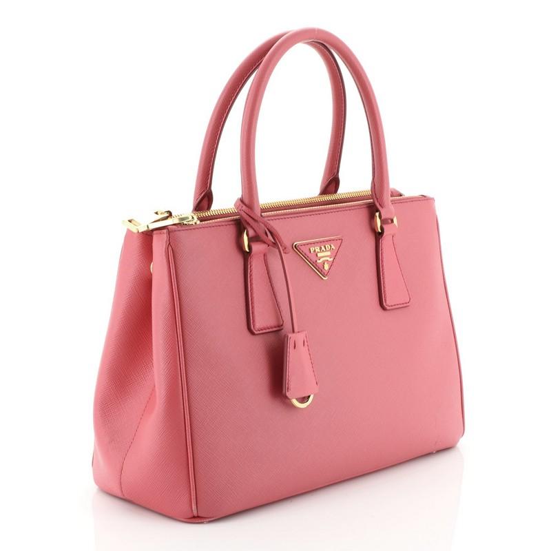 This Prada Galleria Double Zip Tote Saffiano Leather Small, crafted from pink saffiano leather, features side snap buttons, raised Prada logo plate, dual rolled leather handles, and gold-tone hardware. It opens to a pink fabric interior with two zip