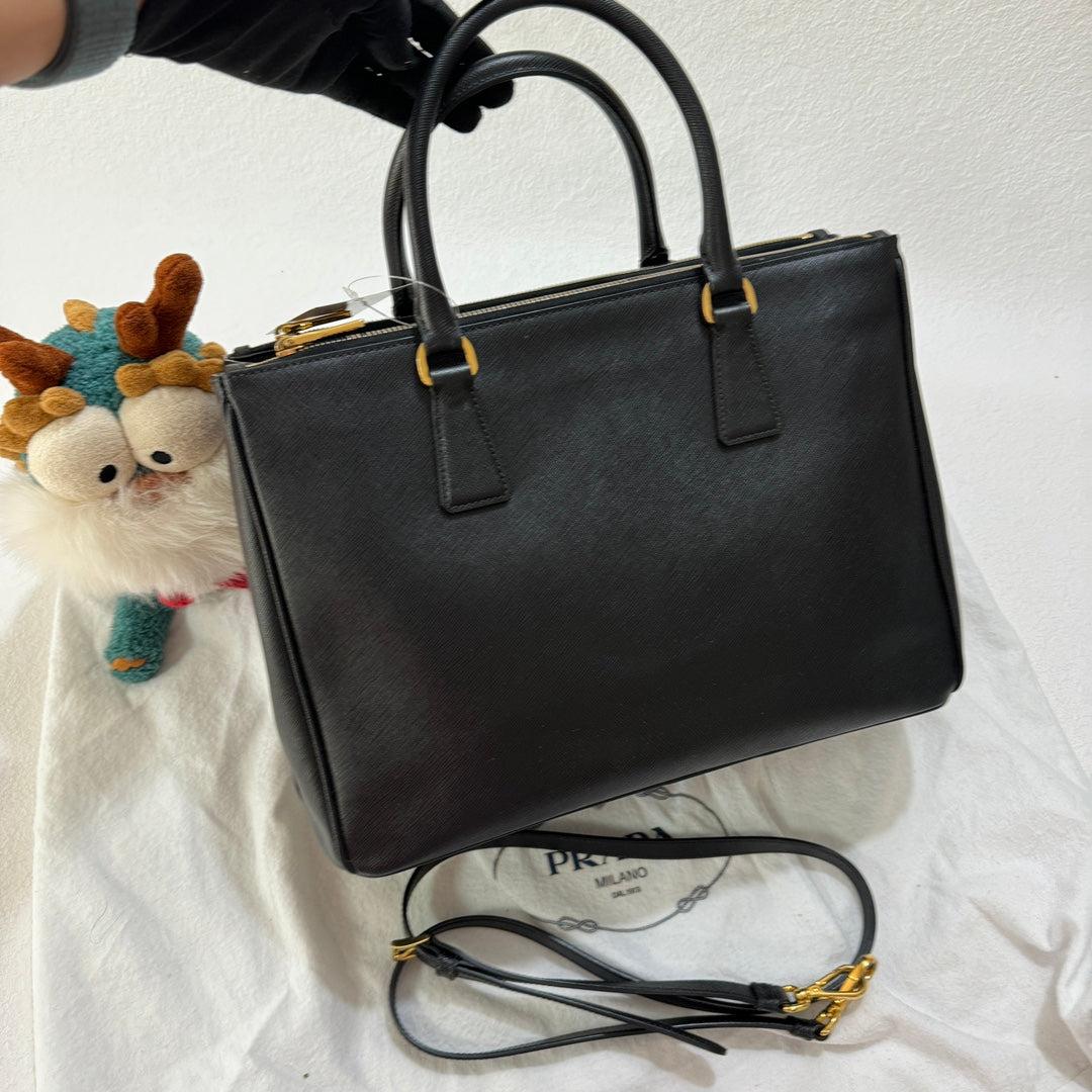 Prada Galleria Saffiano Leather Medium Black Handbag 33cm
 These are professional photos of the actual bag.
 Condition: EXCELLENT
 DETAILS
 
 Prada
 Galleria
 Material: Saffiano calfskin leather
 
 Color: BlackHardware Color: Gold
 Size: