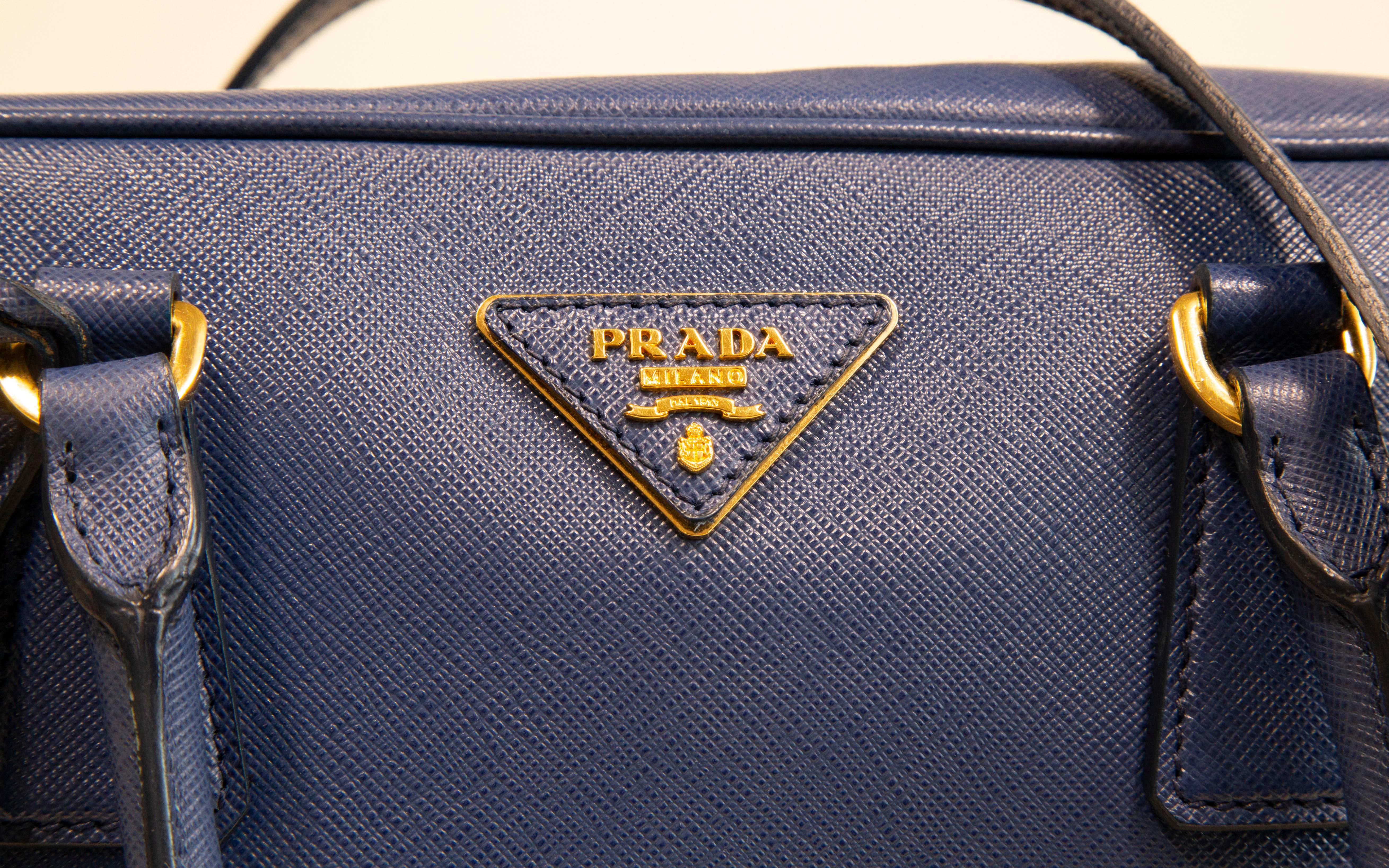 A Prada two way bag made of blue saffiano leather with gold toned hardware, The interior is lined with Prada logo synthetic fabric and next to the major compartment it features four side pockets of which one has a zipper. The bag can be worn as a