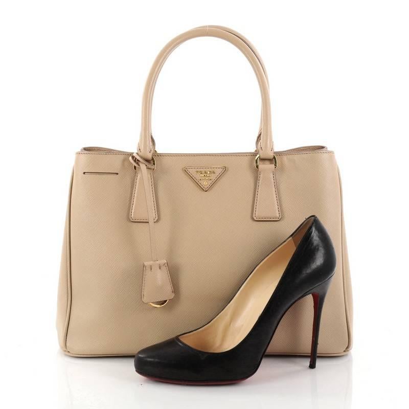 This authentic Prada Gardener's Tote Saffiano Leather Medium is elegant in its simplicity and structure. Crafted from beige saffiano leather, this tote features dual-rolled leather handles, raised Prada logo, protective base studs, and gold-tone