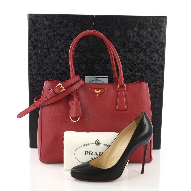 This Prada Gardener's Tote Saffiano Leather Medium, crafted from red saffiano leather, features dual rolled leather handles, raised Prada logo, and gold-tone hardware. Its magnetic snap closure opens to a red nylon interior divided into two