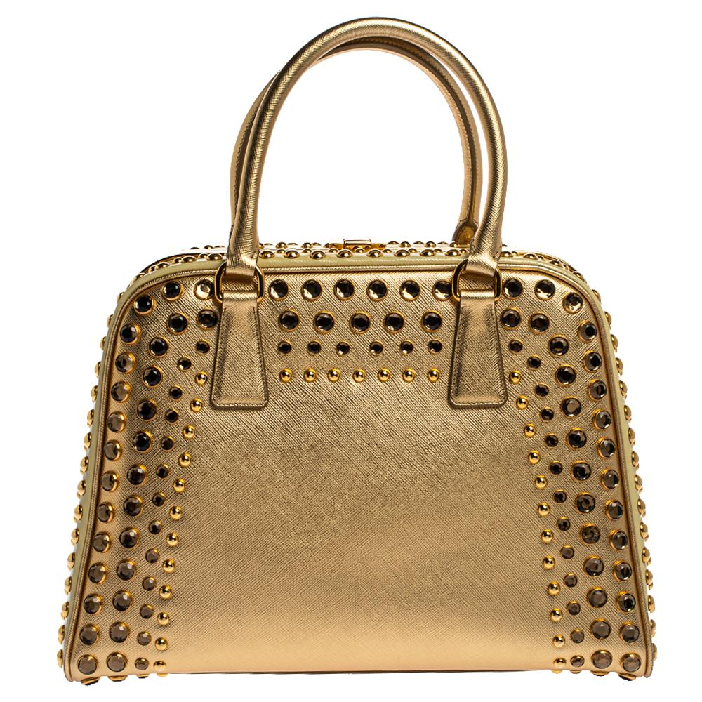 High in appeal and style, this satchel is a Prada creation. It has been crafted from Saffiano lux leather and shaped to exude class and luxury. The bag is adorned with gold-tone studs and comes with two handles and a spacious leather interior for