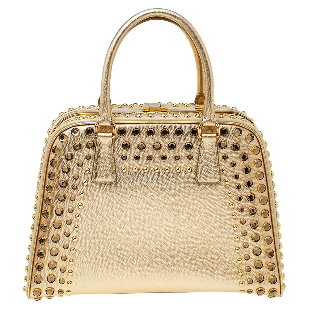 High in appeal and style, this satchel is a Prada creation. It has been crafted from Saffiano lux leather and shaped to exude class and luxury. The bag is adorned with gold-tone studs and comes with two handles and a spacious leather interior for