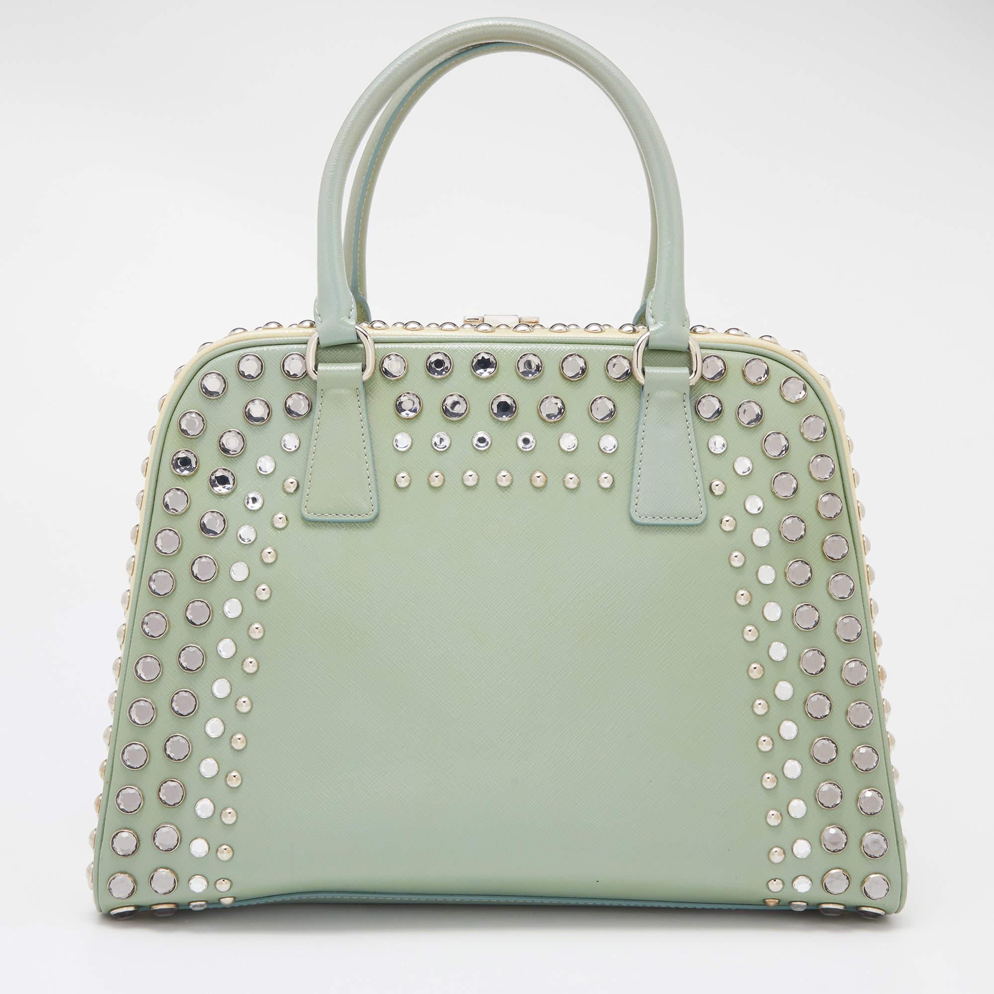 Giving handle bags an elegant update, this Pyramid Frame satchel by Prada aims to be a valuable addition to your closet. It is crafted from Saffiano patent leather and styled with studded embellishments. It comes with dual top handles, protective
