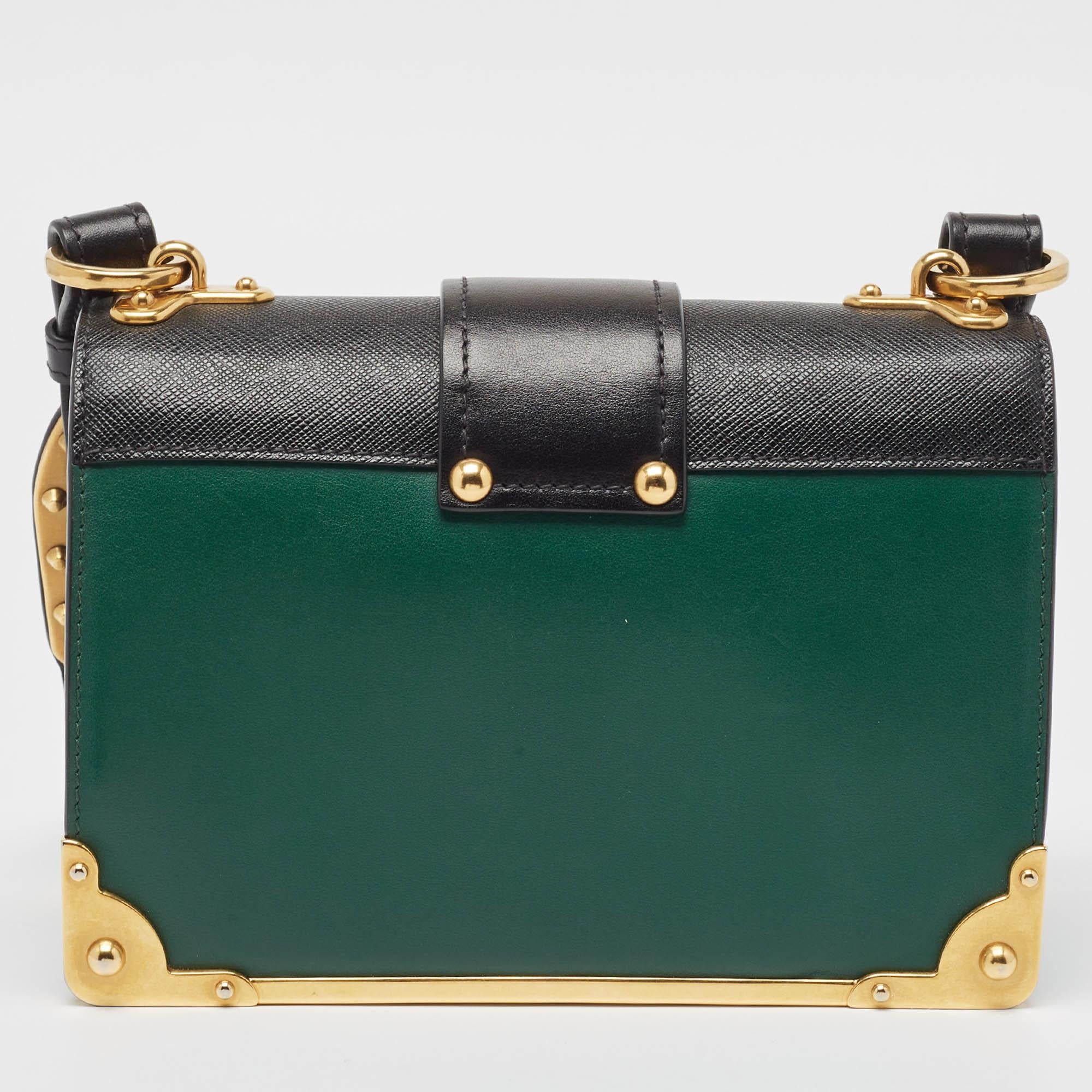Inspired by valuable books from ancient times, the Cahier by Prada is a best-seller. This shoulder bag is crafted in Italy with black and green leather. It features gold-tone trims that add a touch of contrast. The strap closure with the brand logo
