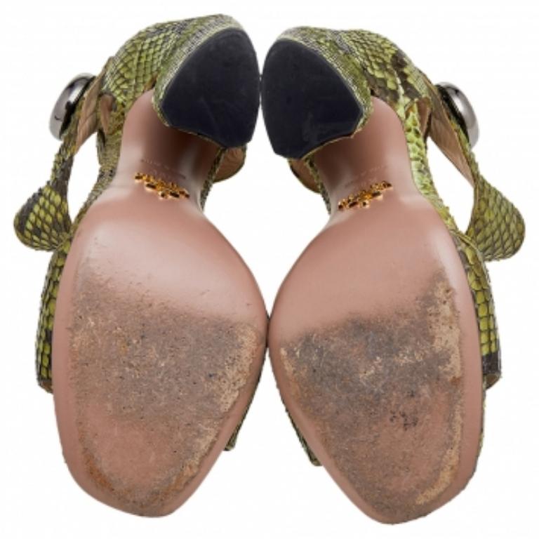Fai ogni passo con sicurezza e disinvoltura con questi splendidi sandali della Maison Prada. Progettati in pelle di pitone verde, questi sandali sono caratterizzati da cinturino alla caviglia, tacco a blocco di 11,5 cm e rifiniture in argento.