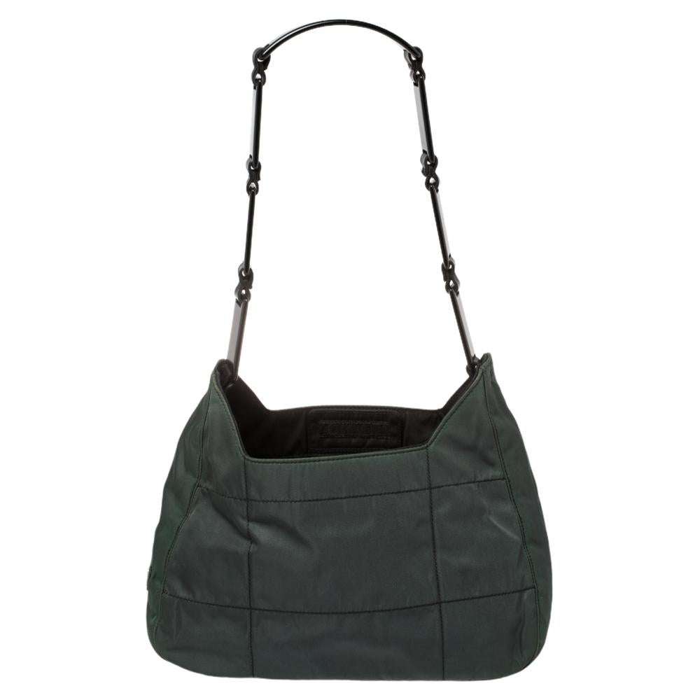 This lovely bag by Prada is meant for everyday use. It has been crafted from quilted fabric and presents itself in a lovely shade of green. It has an open top that leads to a nylon interior, the logo on the sides, and black-tone hardware. It is