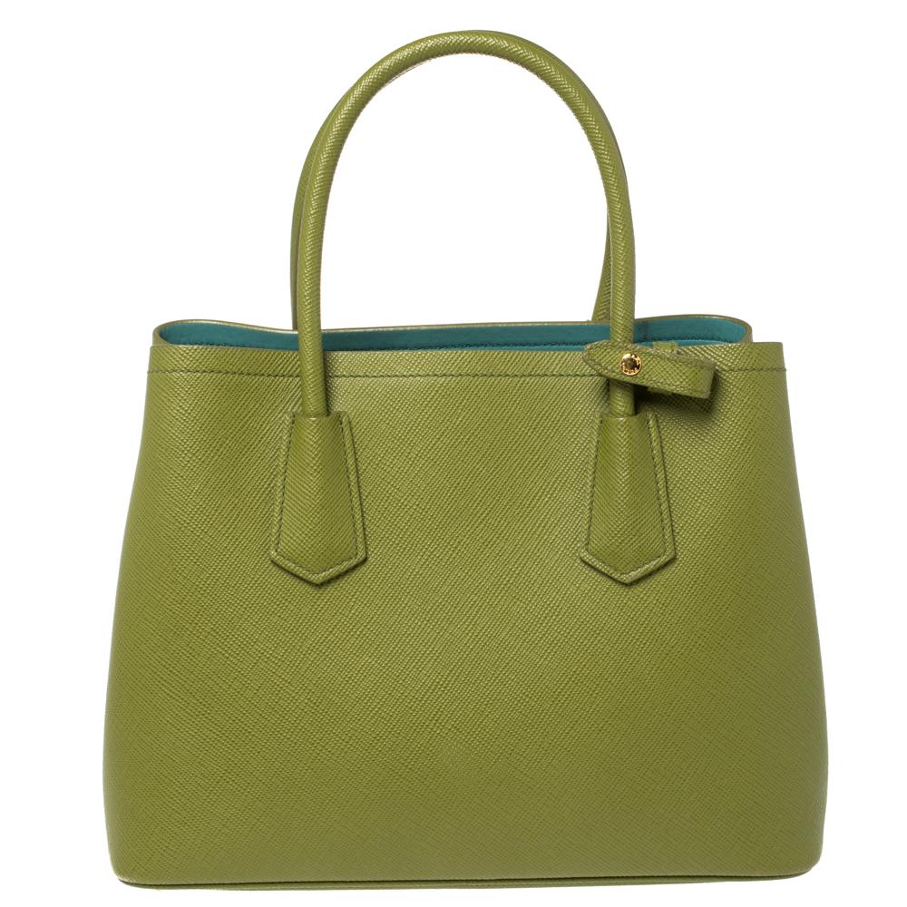 This lovely tote from Prada is crafted from Saffiano Cuir leather and features an alluring green shade. It flaunts dual round handles, an attached clochette, protective metal feet, and a spacious leather-lined interior. Perfect to complement most of