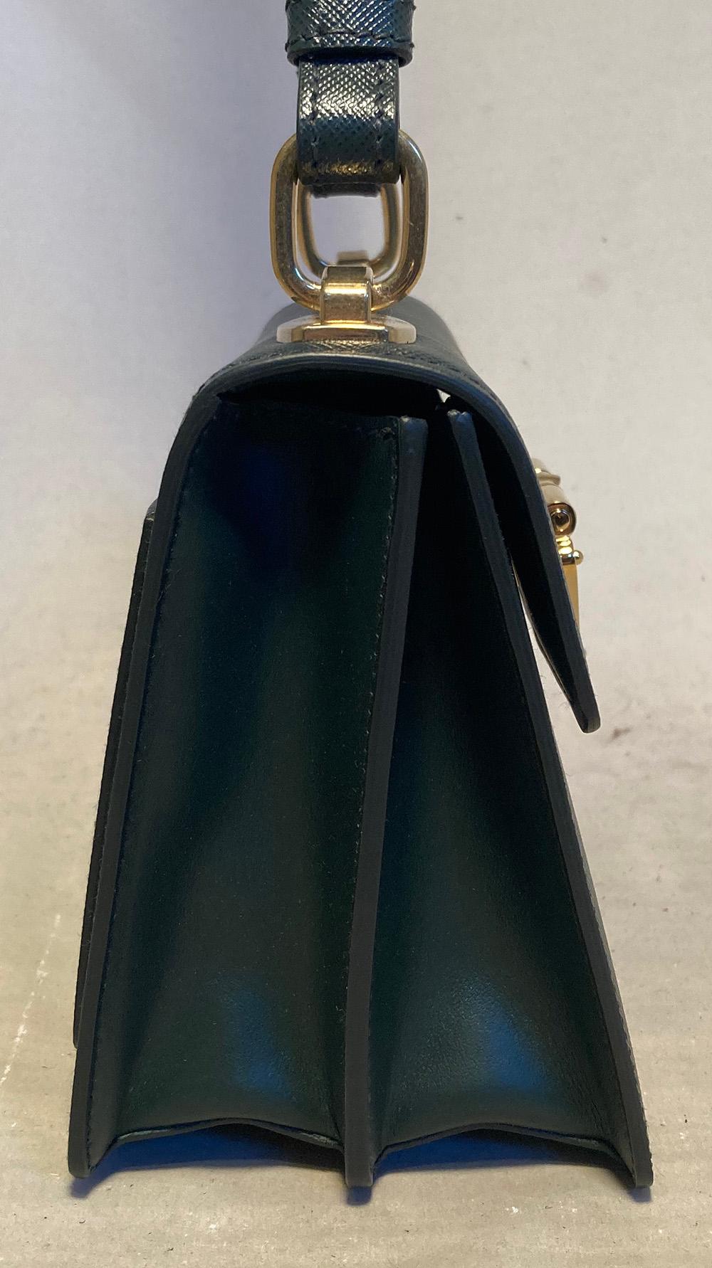 New without tags. grained saffiano leather in dark emerald green trimmed with gold hardware and back side slit pocket. signature triangle logo latch closure opens single flap style to a matching green leather interior with 2 separate compartments.