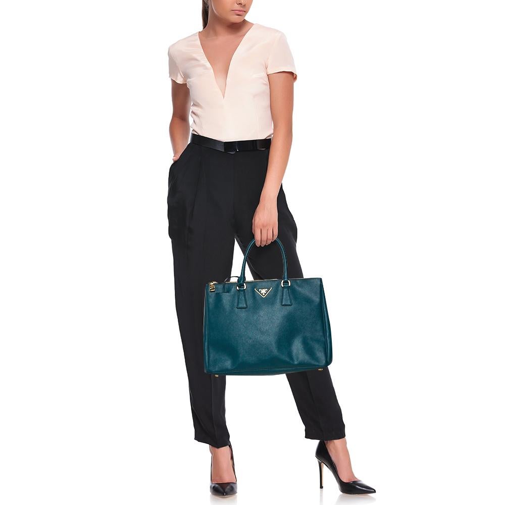 Feminine in shape and grand on design, this Double Zip tote by Prada will be a loved addition to your closet. It has been crafted from Saffiano leather and styled minimally with gold-tone hardware. It comes with two top handles, two zip