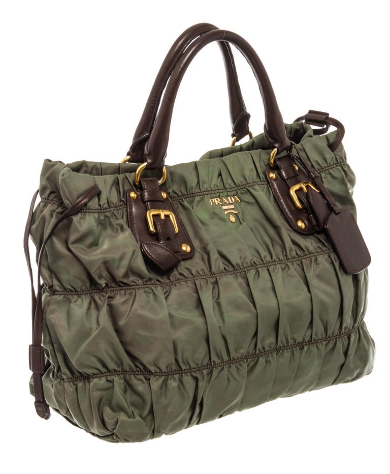 Prada Gaufre tote bag features a gathered green nylon body, two rolled leather handles, gold-tone hardware, a detachable flat leather strap, a top magnetic closure, side laces that cinch, brown Jacquard canvas lining and slip pockets inside.

