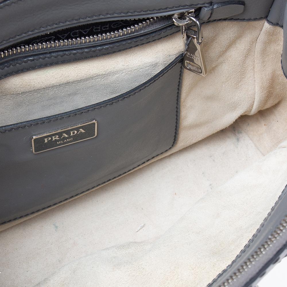 One of the most prestigious and iconic creations of the House of Prada is this stunning Double Zip tote. It is made from grey leather on the exterior, with a logo detail highlighting the front. It features silver-toned hardware and a fabric-lined