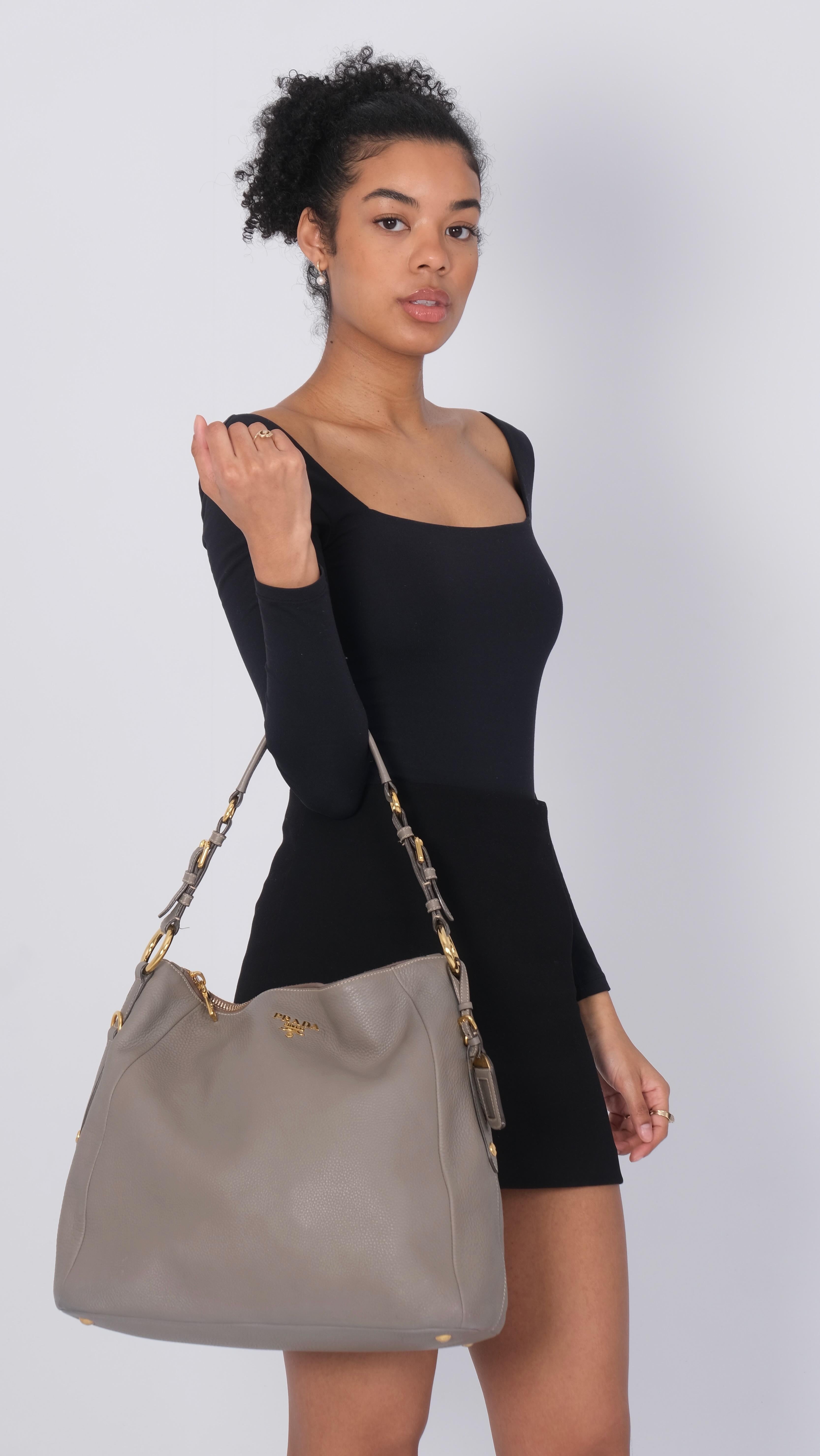 This hobo bag is made of textured calfskin leather in grey. This bag features a looping leather top handle, polished gold hardware including the expanding side zippers, and the classic polished gold metal 