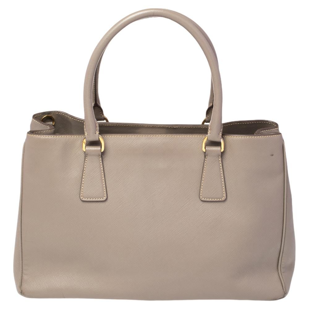 Loved for its classic appeal and functional design, Galleria is one of the most iconic and popular bags from the house of Prada. This beauty in grey is crafted from Saffiano leather and is equipped with two top handles, the brand logo at the front