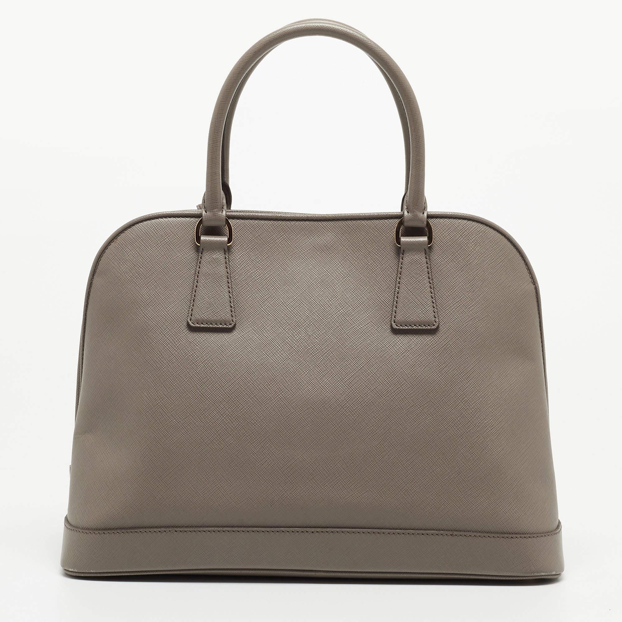 With a well-structured shape, this Prada bag embodies sophistication and style. Crafted from Saffiano lux leather, it flaunts top dual handles, a brand signature on the front, and gold-tone hardware. The nylon and leather lined interior is secured