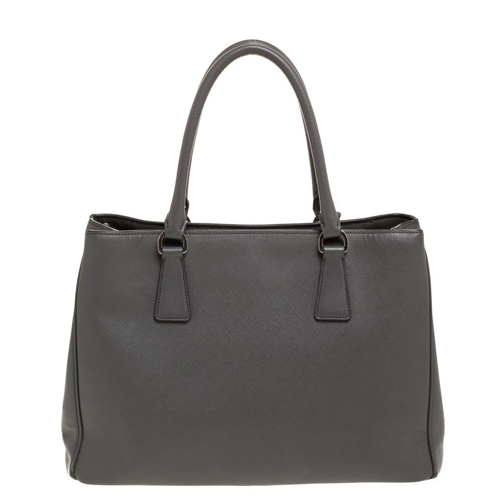 Feminine in shape and grand on design, this Double Zip tote by Prada will be a loved addition to your closet. It has been crafted from Saffiano Lux leather and styled minimally with gold-tone hardware. It comes with two top handles, two zip