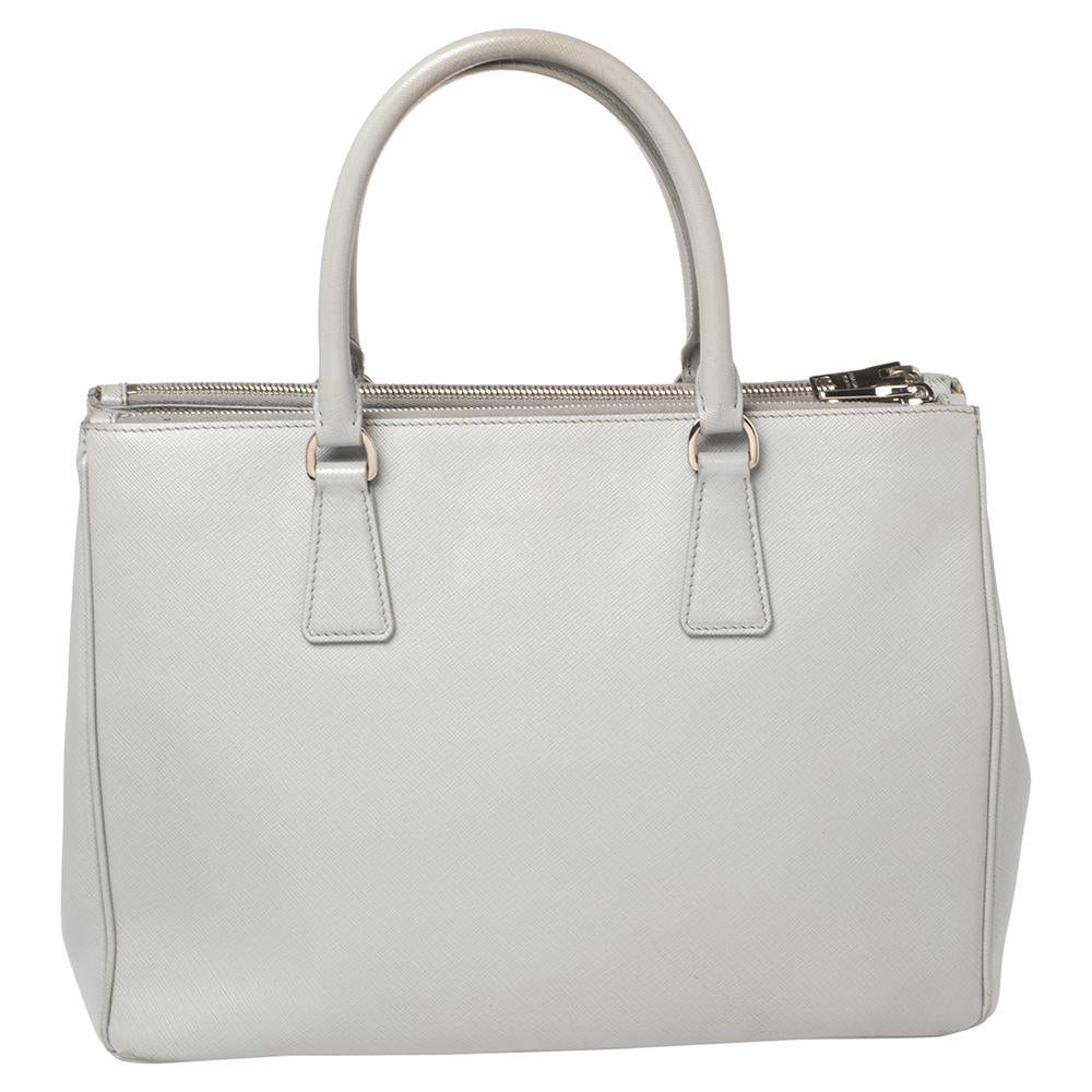 Loved for its classic appeal and functional design, Galleria is one of the most iconic and popular bags from the house of Prada. This beauty in grey is crafted from Saffiano Lux leather and is equipped with two top handles, the brand logo at the