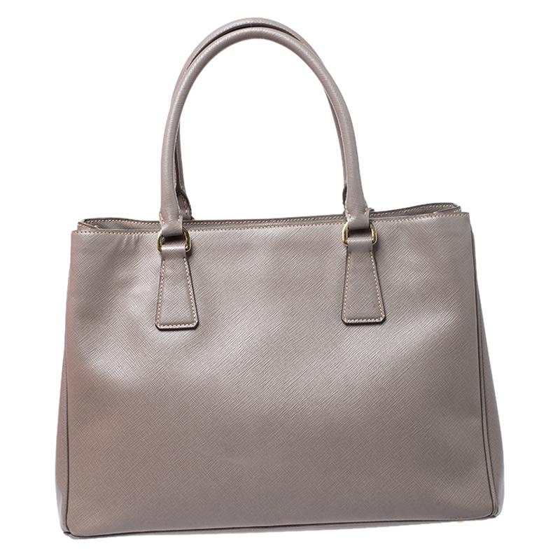 This tote by Prada will be a loved addition to your closet. It has been crafted from Saffiano Lux leather and styled minimally with gold-tone hardware. It comes with two top handles and a nylon interior divided by a zip compartment. The bag is
