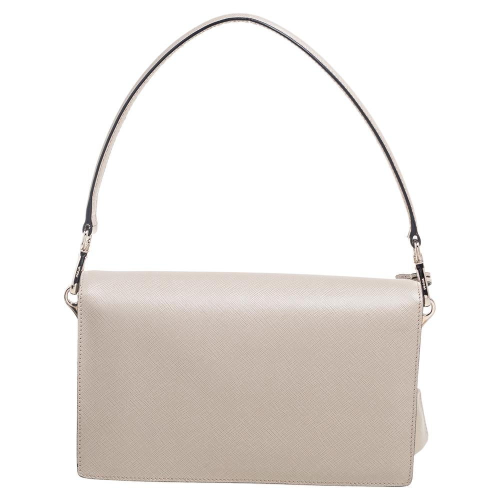 Give your handbag collection a makeover with this spectacular bag from the House of Prada! It is made from grey Saffiano Lux leather on the exterior with a logo-engraved lock closure perched on the front. It has a sturdy top handle, a leather-lined
