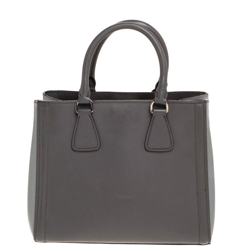 This elegant tote from Prada is crafted from Saffino Lux leather and is perfect for daily use. The bag features double handles, protective metal feet, and a leather tag to the front. The bag opens to a nylon-lined interior. The grey-hued tote is