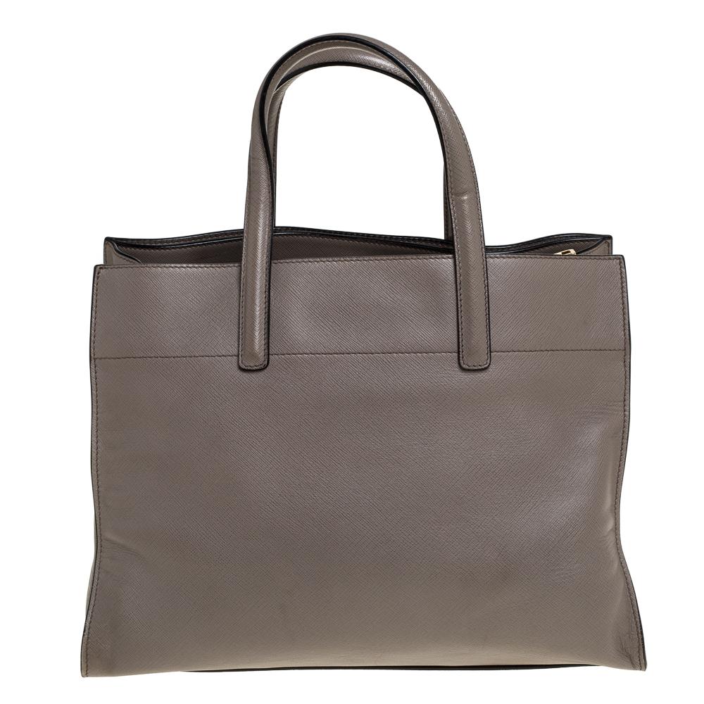 Created from grey Saffiano leather and lined with leather and nylon, this Prada bag is a fine accessory for all your needs. The tote has spacious compartments and two handles for you to parade the beauty. It is stylish, functional and