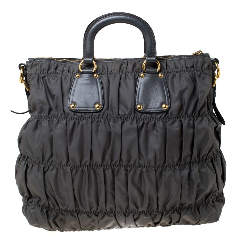 This Prada tote has a style of its own, designed with ruched and pleated rows that add a summery touch. Made from nylon, it features leather trims with double top handles, a removable shoulder strap, and an ID tag with a clear window. The gold-tone