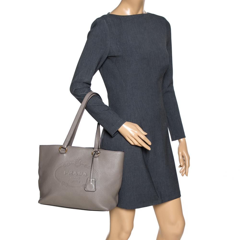 This lovely tote from Prada is crafted from Vitello Daino leather and features a grey shade. It flaunts dual handles, the logo embossed on the front, protective metal feet, and a spacious nylon-lined interior. Perfect to complement most of your